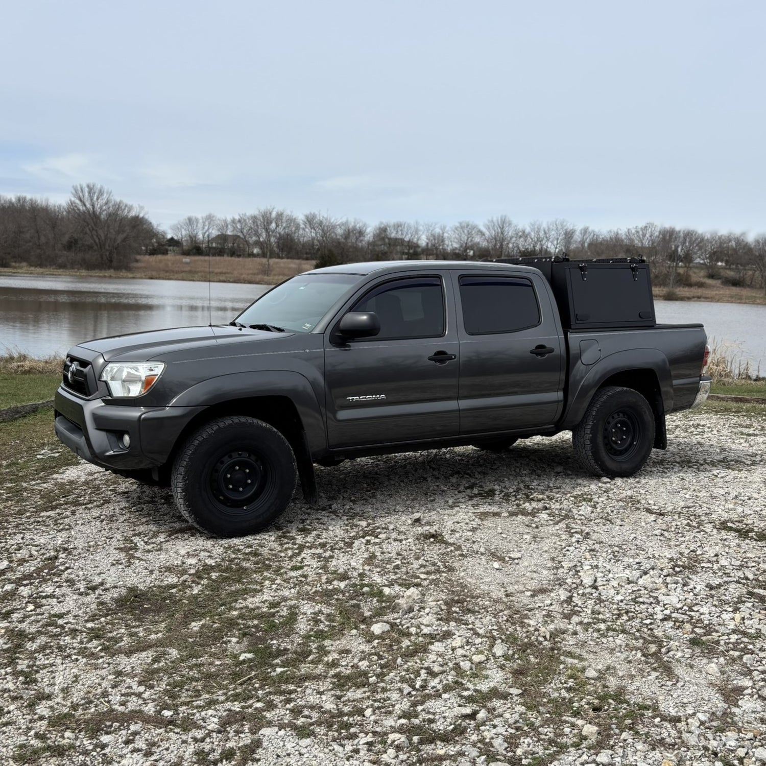 Grey Toyota Tacoma overland truck with toolboxes in nature by a lake.