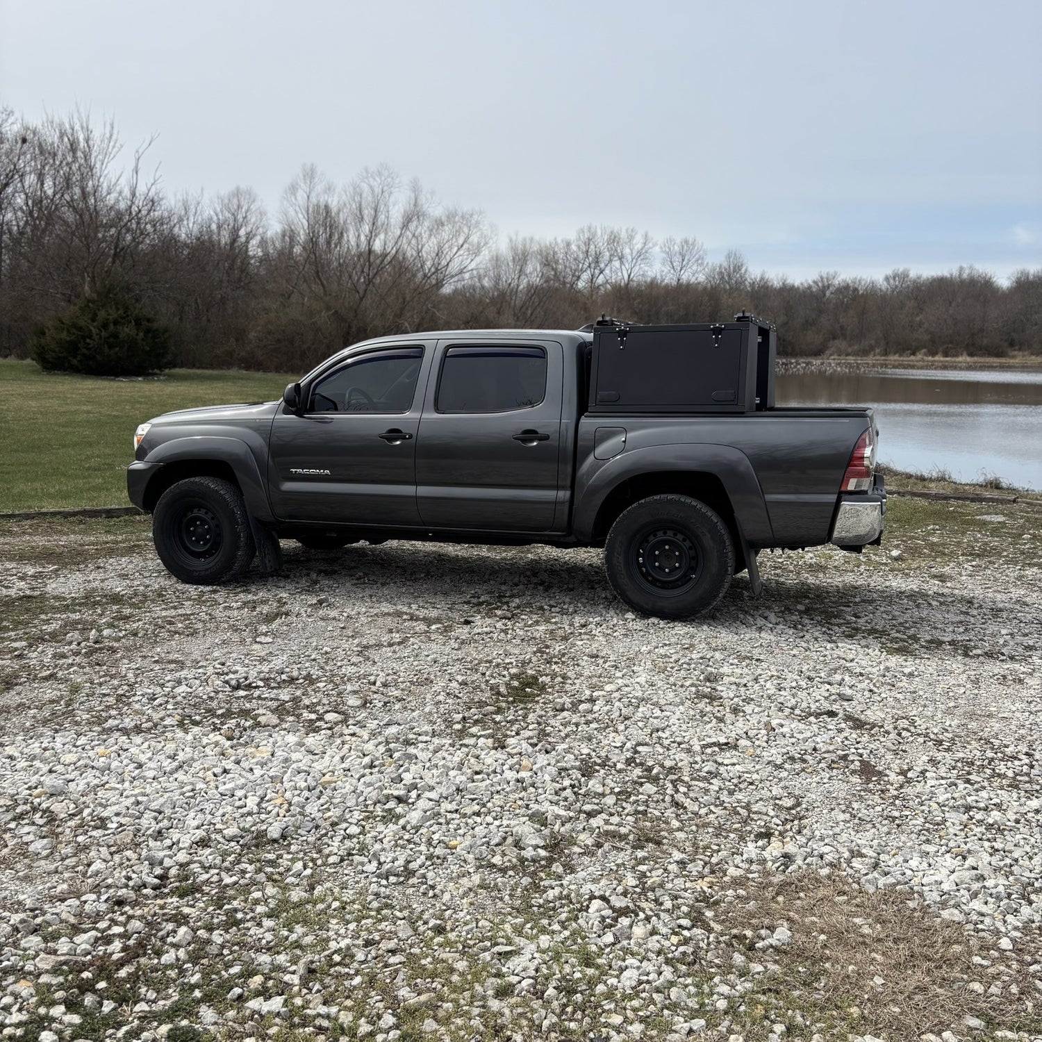 Grey Toyota Tacoma overland truck with toolboxes in nature by a lake.