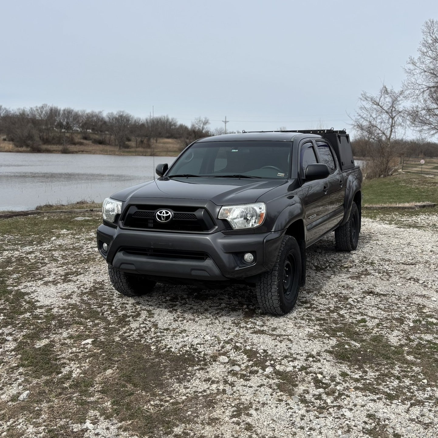 Grey Toyota Tacoma overland truck with toolboxes in nature by a lake.