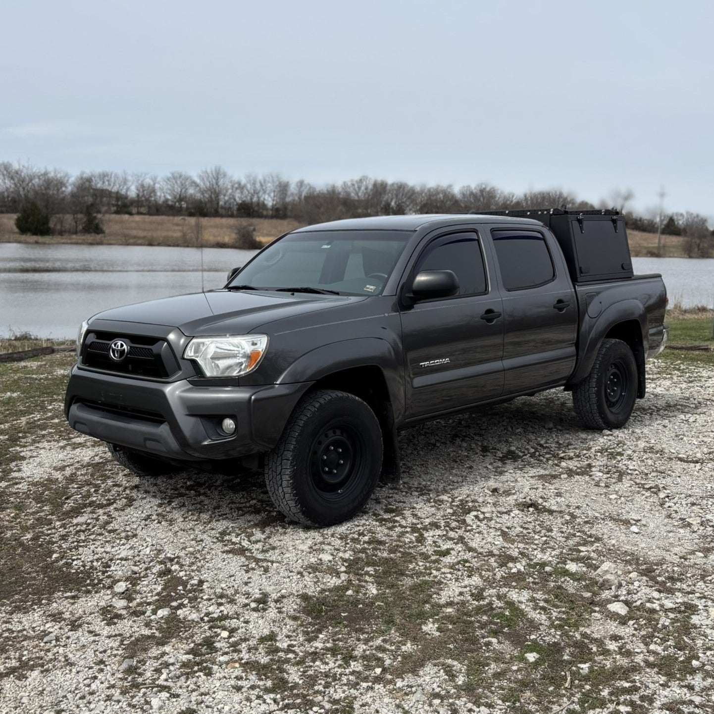 Grey Toyota Tacoma overland truck with toolboxes in nature by a lake.