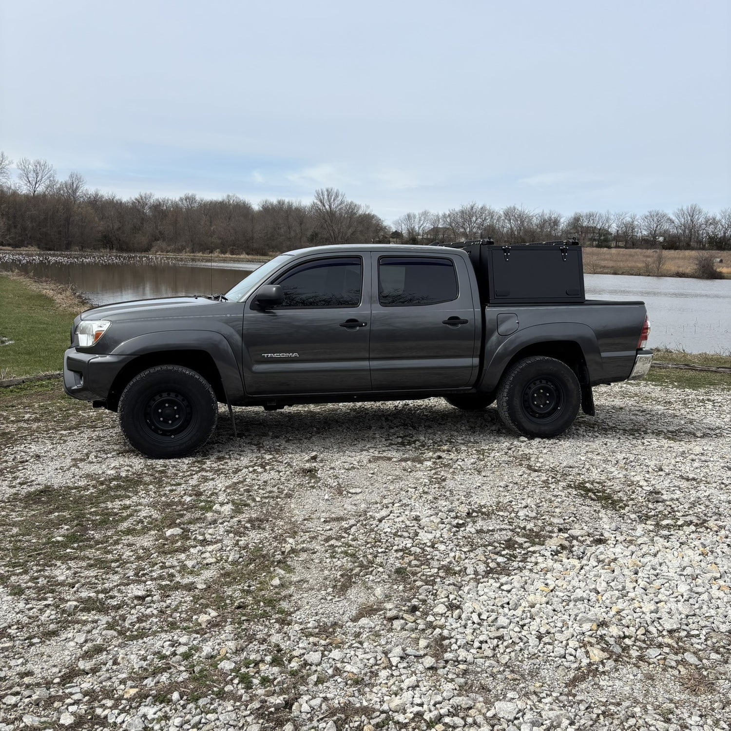 Grey Toyota Tacoma overland truck with toolboxes in nature by a lake.