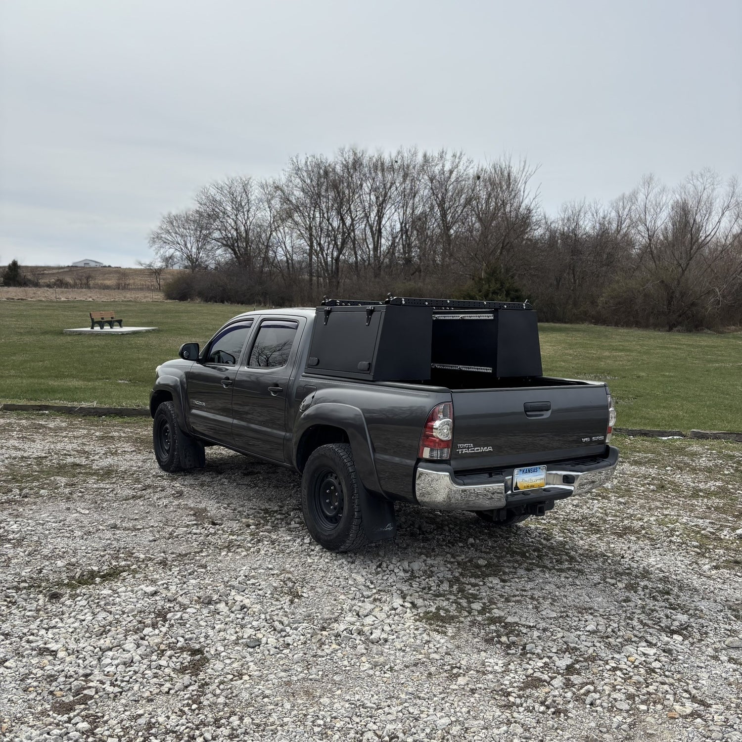 Grey Toyota Tacoma overland truck with toolboxes in nature by a lake.